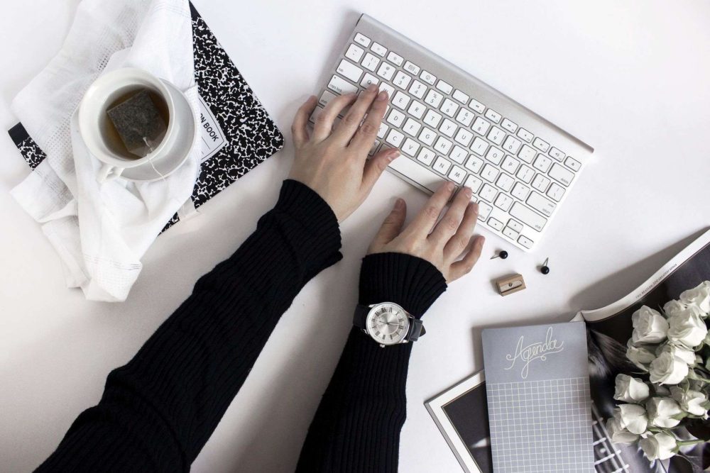 Girl typing on Keyboard with coffee cup - How to start a blog in 10 simple steps - Blogging for Beginners